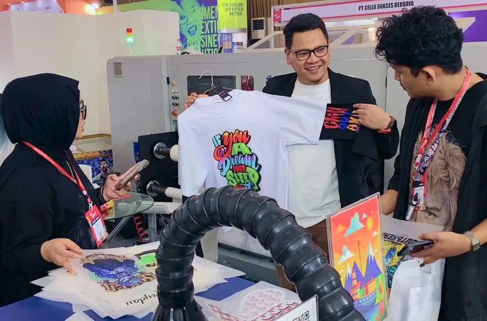 Tim sedang berdiskusi di depan mesin cetak kaos digital sebagai gambaran kebutuhan memulai bisnis digital printing.