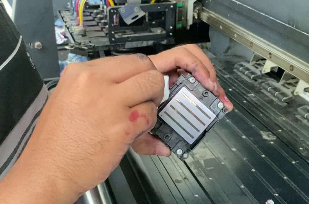Teknisi membersihkan printhead printer sublim untuk mencegah nozzle mampet saat produksi cetak jersey.